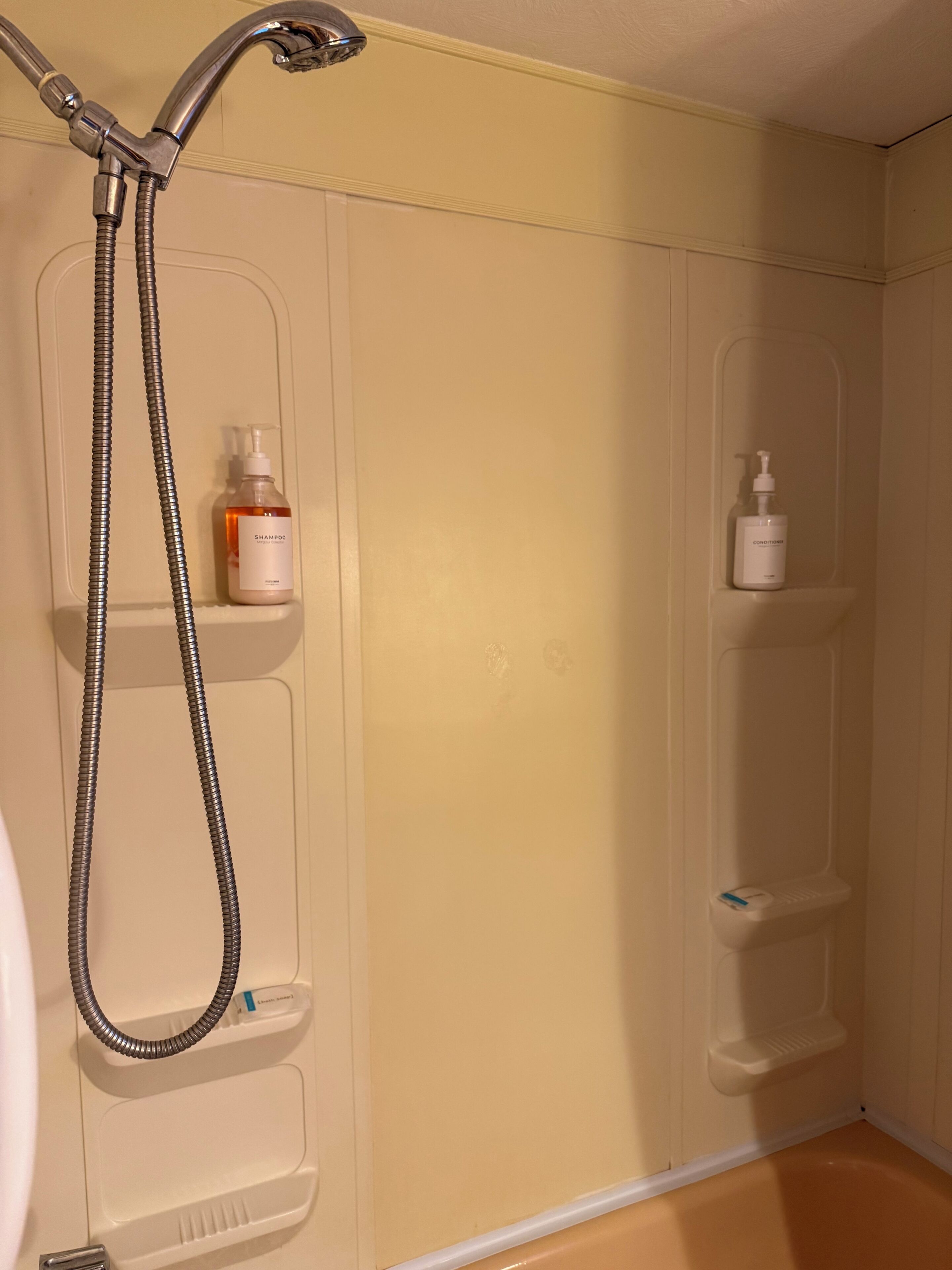 A bathroom with a shower, two shelves with toiletries, and a white wall.