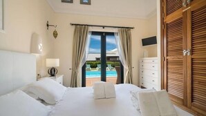 Habitación de hotel con cama, mesita de noche, lámpara, armario de madera y vista a una piscina.