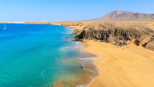 A coastal landscape with clear blue waters, sandy beach, and rocky cliffs. - *Luxury Villa* | Heated Pool, Sea & Mountain Views - High Speed WIFI. (Playa Blanca)