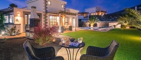 A modern house with a patio, two wicker chairs, and a small table with drinks.