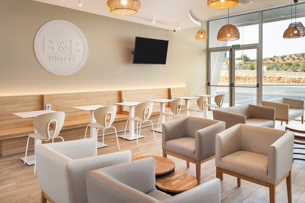 A modern hotel lobby with a large TV, comfortable seating, and a view of the outdoors.