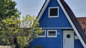 Una casa azul con tres ventanas y una puerta blanca, rodeada de un césped cuidado y un árbol.