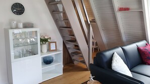 Una sala de estar moderna con una escalera, un mueble blanco con estantes de vidrio, un sofá de cuero negro y un reloj en la pared.