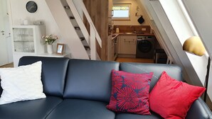 Una sala de estar moderna con un sofá de cuero negro, un mueble blanco con puertas de vidrio y una escalera que da a una zona de cocina.