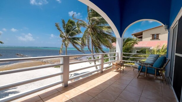 A balcony with a view of the beach and ocean, featuring a railing, a chair, and a small table. - Beach and Oceanfront apartment Casa Mar Y Sol (San Pedro)