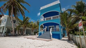 A two-story building with a blue facade and white railings, situated on a sandy beach with palm trees. - Beach and Oceanfront apartment Casa Mar Y Sol (San Pedro)