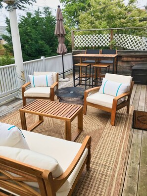 A wooden deck with outdoor furniture, including chairs and a table, and a white fence in the background. - Hummingbird Cottage with Park Views, Pet-Friendly (Cape Charles)