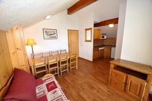 A cozy room with a wooden floor, a red sofa, a dining table with chairs, and a kitchen area with wooden cabinets and a microwave. - Ski-in/ski-out & foot of the slopes, balcony, tv, 35m², Puy-Saint-Vincent (Puy-Saint-Vincent)