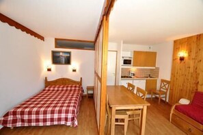 A compact room with a bed, a wooden table, and a kitchenette. - Ski-in/ski-out & foot of the slopes, balcony, tv, 30m², Puy-Saint-Vincent (Puy-Saint-Vincent)