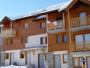 A multi-story wooden building with balconies, stone accents, and a snow-covered roof. - Ski-in/ski-out & foot of the slopes, balcony, tv, 30m², Puy-Saint-Vincent (Puy-Saint-Vincent)