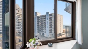 Una ventana con vista a un edificio moderno identificado como "FLYING CLOUD" y una pequeña planta en maceta en el alféizar.