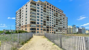 Un edificio residencial de varios pisos con balcones, un sendero de arena y una valla de madera.