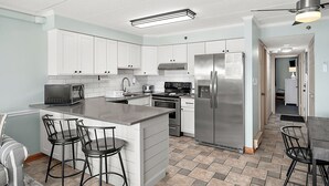 Una cocina moderna con armarios blancos, electrodomésticos de acero inoxidable y una isla central con taburetes de bar.