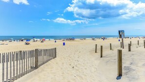 Una playa con una valla de madera, sombrillas y gente.