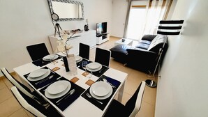 Et spiseområde med et bord dækket til fire personer, en sofa, et fjernsyn og et spejl på væggen.