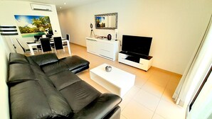 En moderne stue med en hjørnesofa, et fladskærms-tv, et sofabord og et spiseområde med stole og bord.