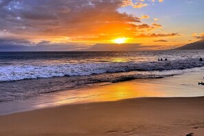 Uma praia com ondas, um pôr do sol e uma montanha ao longe.