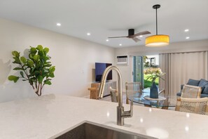 Uma cozinha moderna com uma torneira de aço inoxidável, uma sala de jantar com mesa de vidro e cadeiras de vime, e um ventilador de teto.