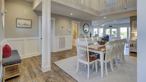 A spacious dining area with a high ceiling, white railings, and a view of the outdoors.