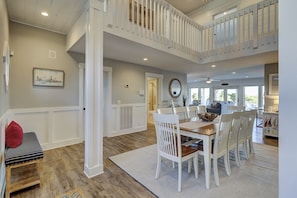 A spacious dining area with a high ceiling, white railings, and a view of the outdoors.
