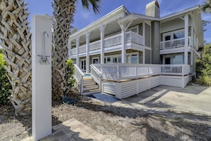 A multi-story beachfront house with a covered porch, a pool, and a staircase leading to the upper levels.