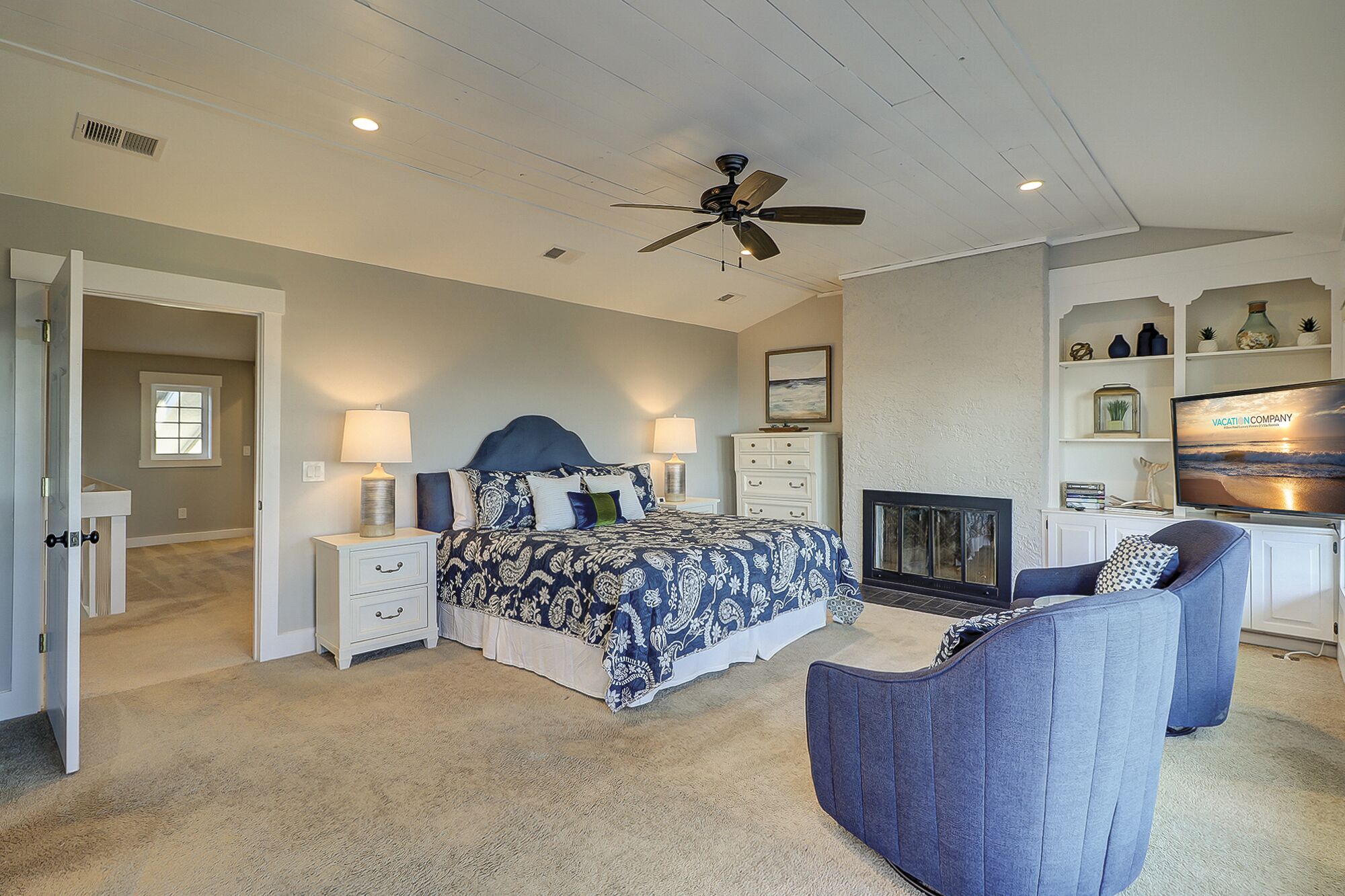 A bedroom with a bed, nightstands, a chair, a fireplace, and a television.