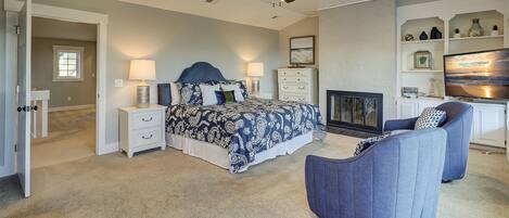 A bedroom with a bed, nightstands, a chair, a fireplace, and a television.