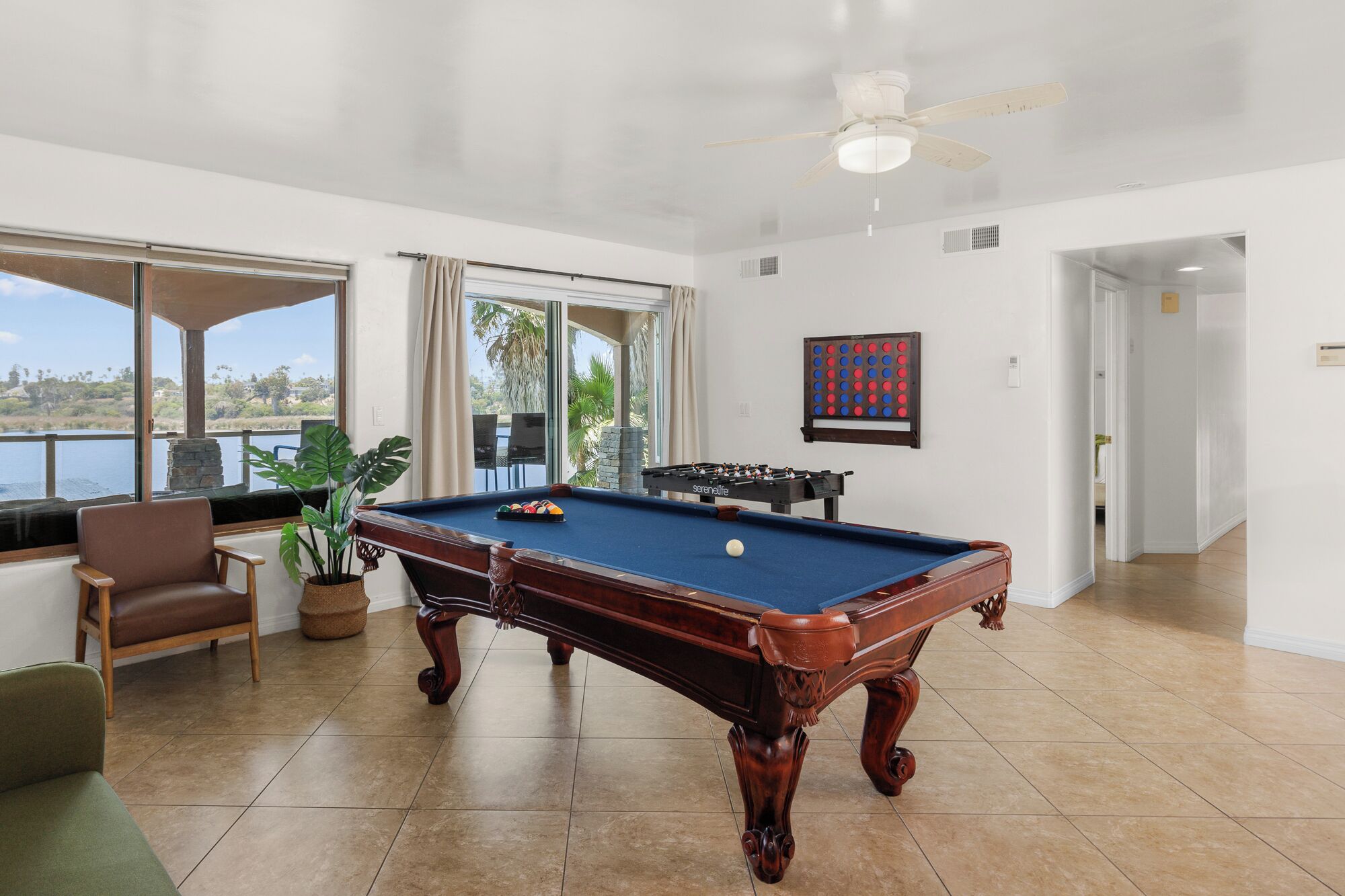 A pool table in a room with a view of the outdoors, a ceiling fan, and a foosball table.