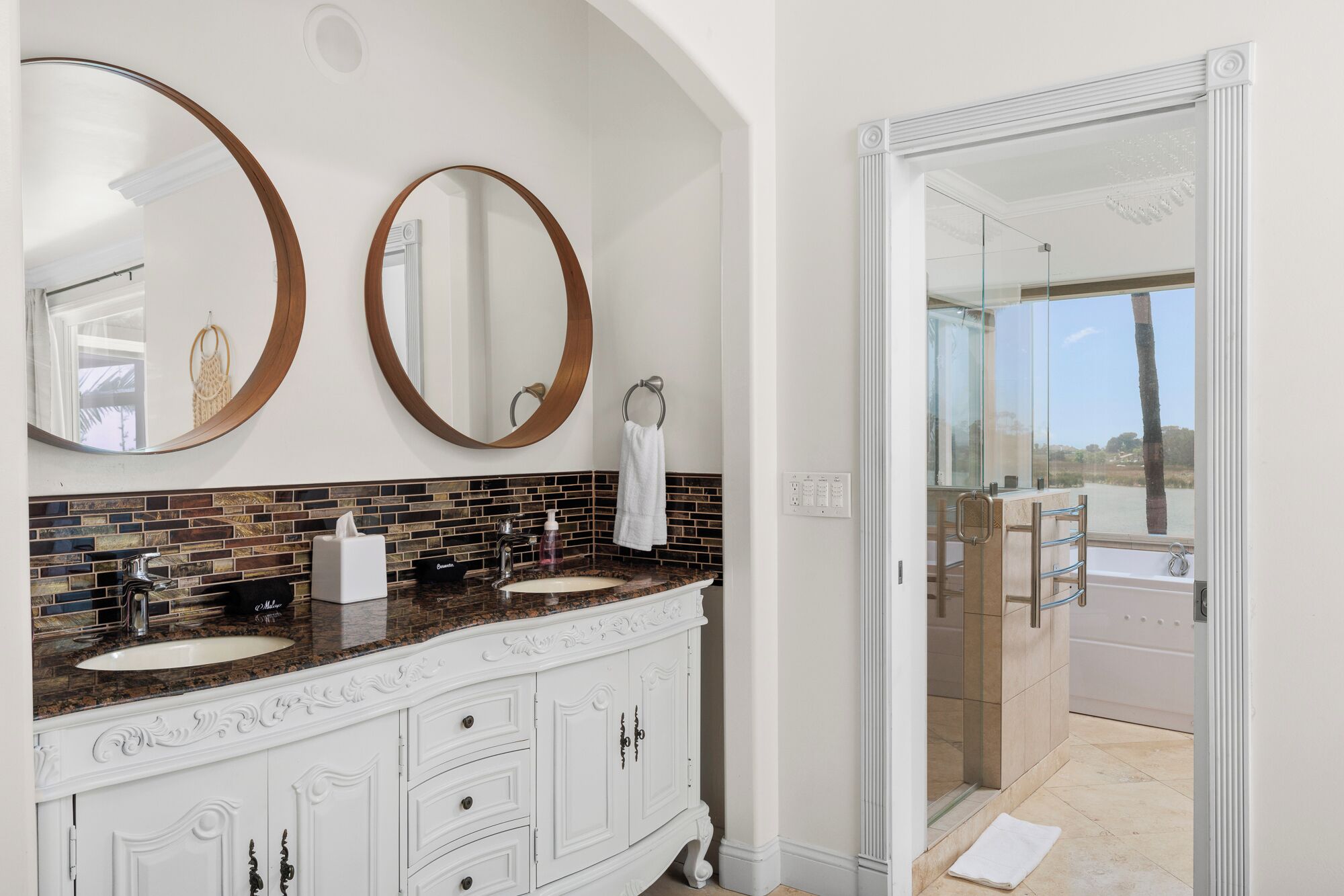 A bathroom with two large mirrors, a marble countertop, and a glass-enclosed shower.