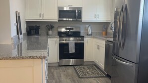 A modern kitchen with white cabinets, stainless steel appliances, and a wooden floor. - Adorable 2 Bedroom Vacation Rental Located on Canal (Algonac)