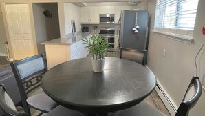 A dining area with a round table, four chairs, a potted plant, and a kitchen in the background. - Adorable 2 Bedroom Vacation Rental Located on Canal (Algonac)