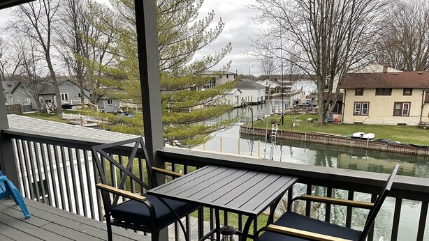 A deck with a table and chairs overlooking a canal with houses in the background. - Adorable 2 Bedroom Vacation Rental Located on Canal (Algonac)