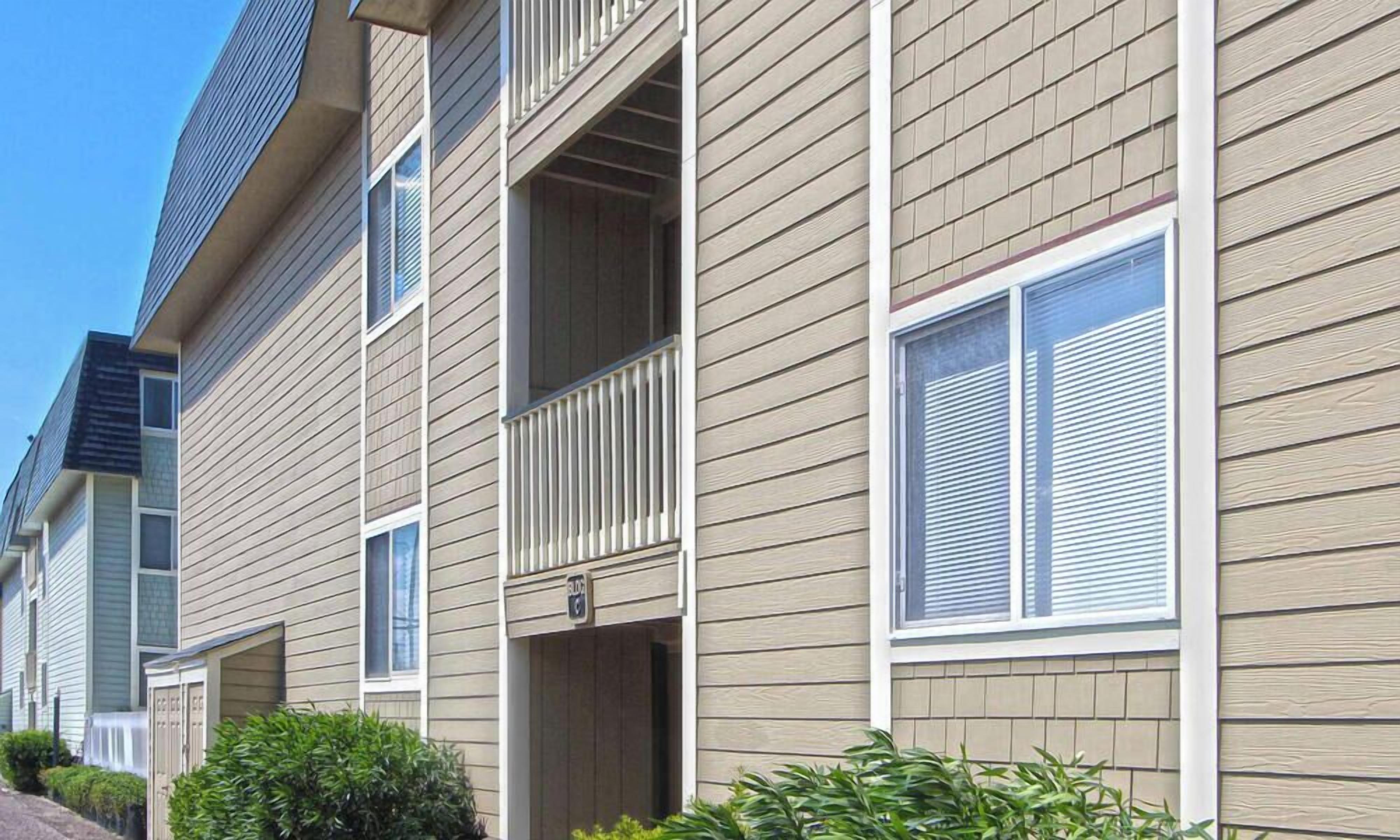 A row of townhouses with beige siding, white shutters, and a small balcony on each unit.