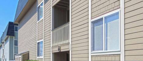 A row of townhouses with beige siding, white shutters, and a small balcony on each unit.