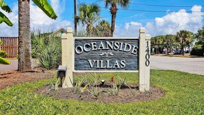 Placa indicando Oceanside Villas, emoldurada por vegetação tropical e céu claro.