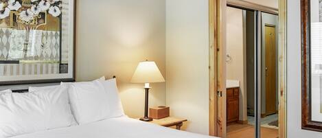 A hotel room with a bed, a bedside lamp, a painting, and a door leading to a bathroom.