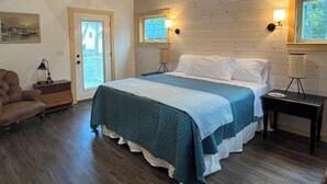 A cozy bedroom with a wooden ceiling, a large bed with a blue and white bedspread, two bedside lamps, and a nightstand. - Next Avail. Aug 22 - 3 night min - AC - Premier Cottage, King Bedroom, Pets Free (Round Pond)