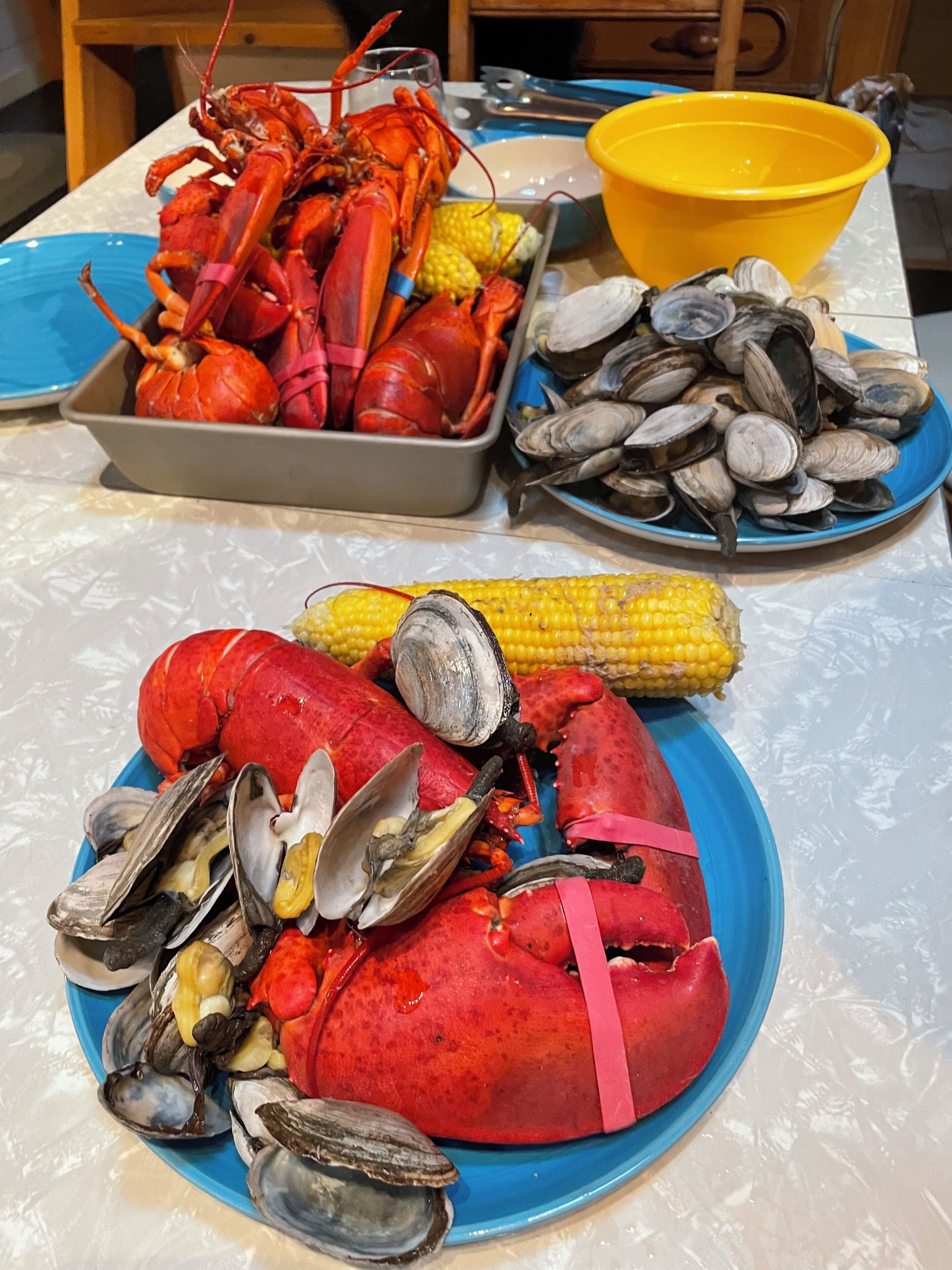 A table with seafood dishes including lobsters, clams, and corn.
