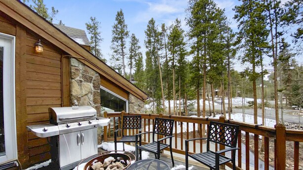 A wooden deck with a grill, outdoor seating, and a stone wall.