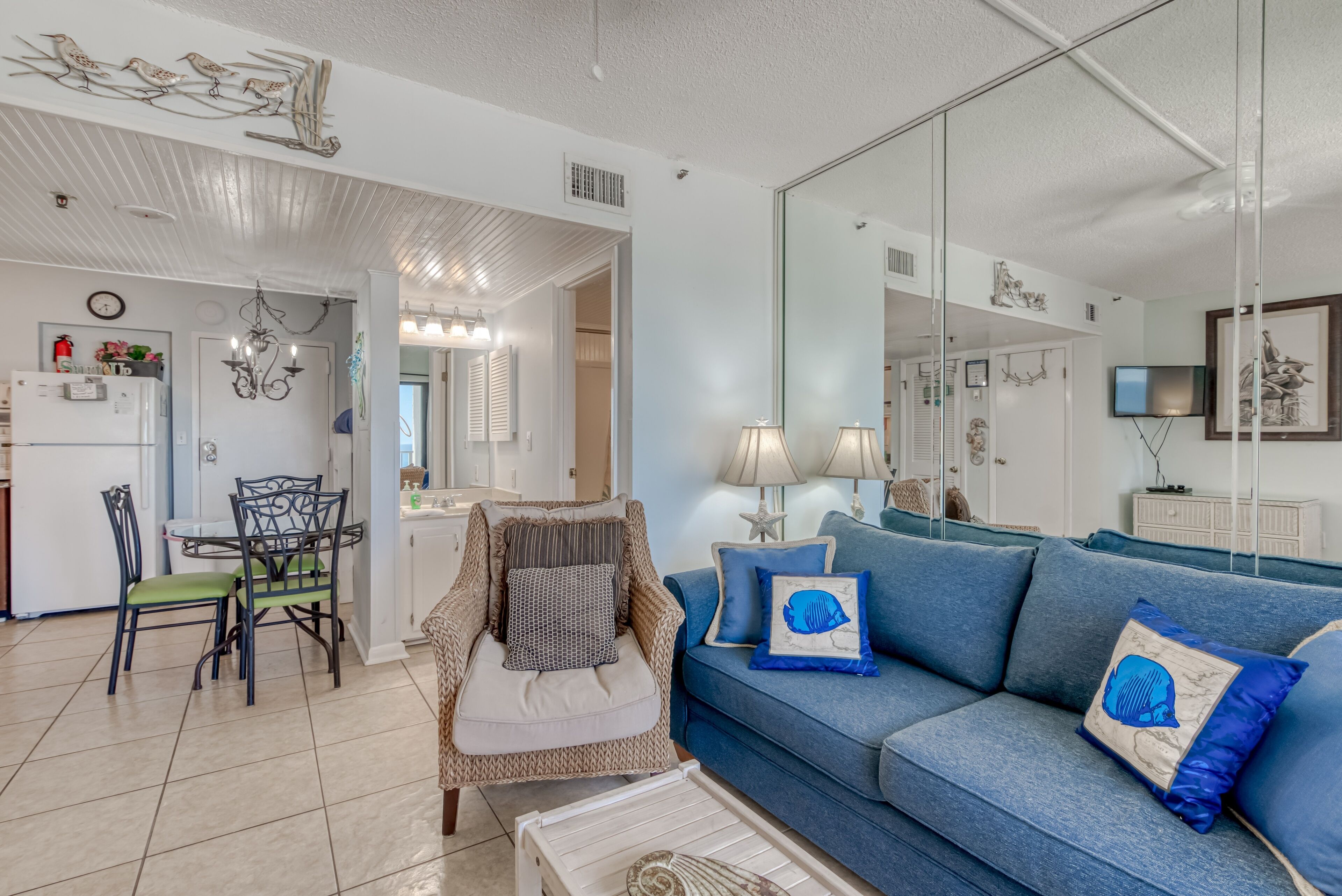 A living room with a blue sofa, a dining table with chairs, a chandelier, and a large mirror.