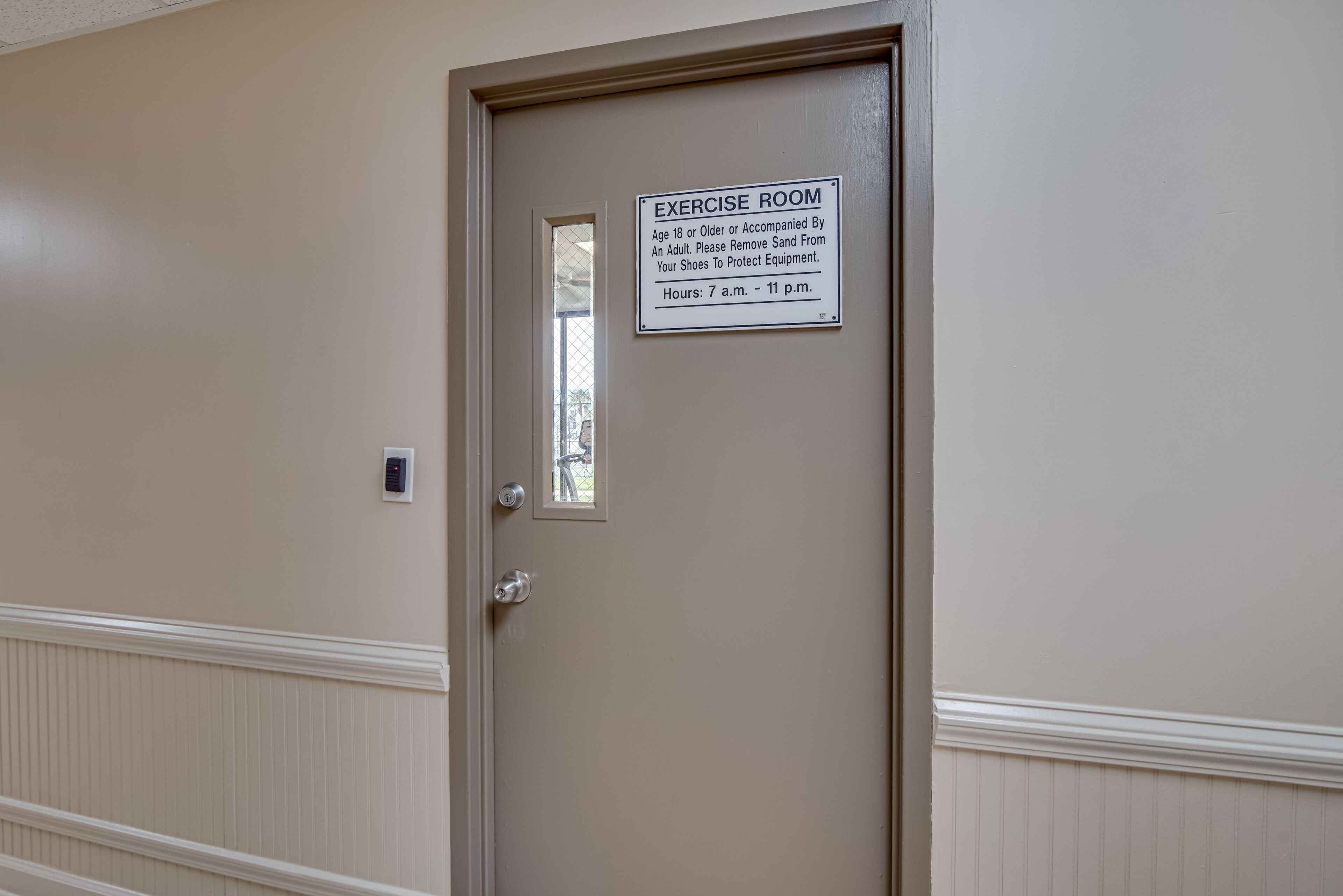 A door with a sign indicating an exercise room, a window, and a wall-mounted light switch.