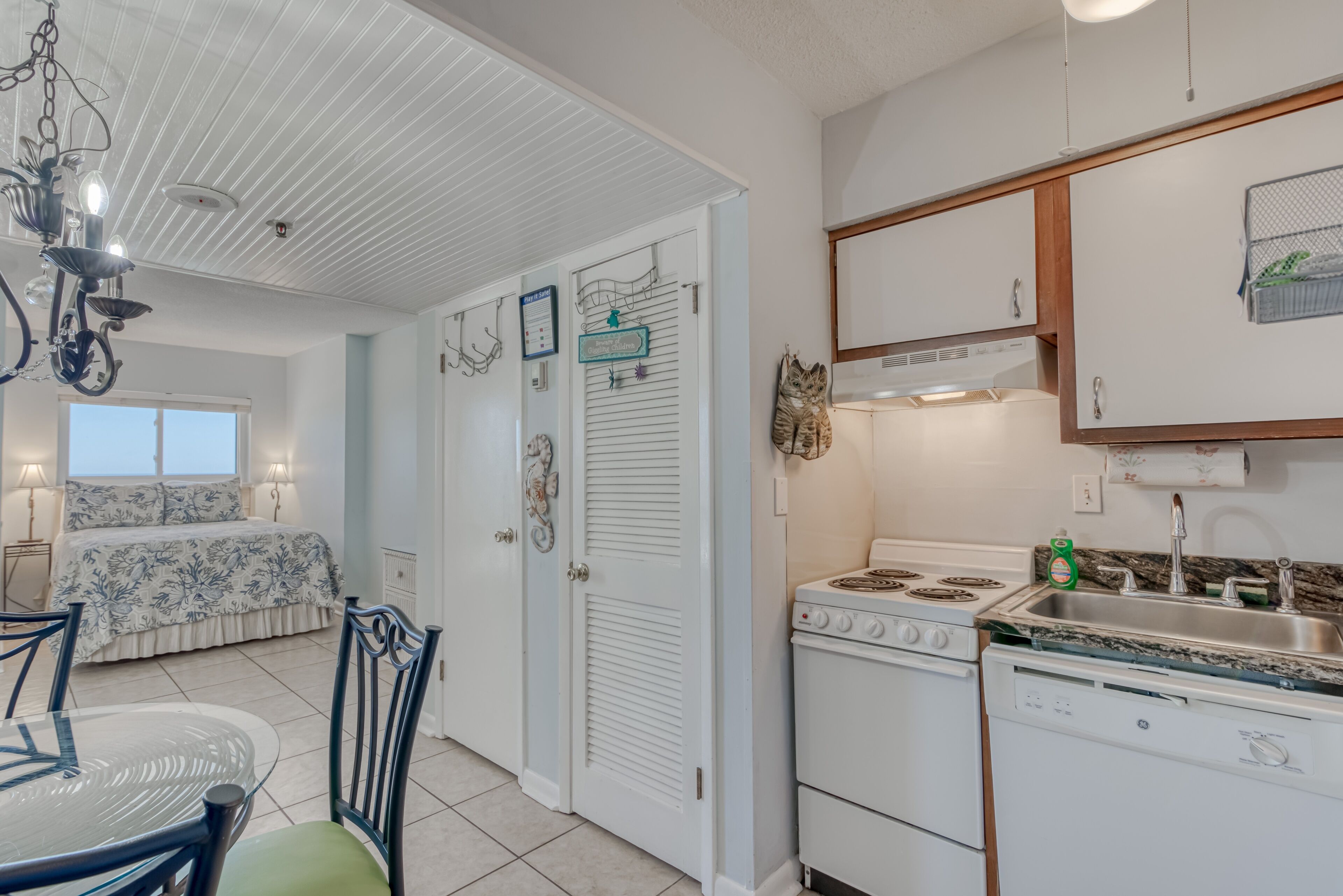 A kitchen with white cabinets, a stove, and a sink. There is a dining table with chairs and a chandelier.