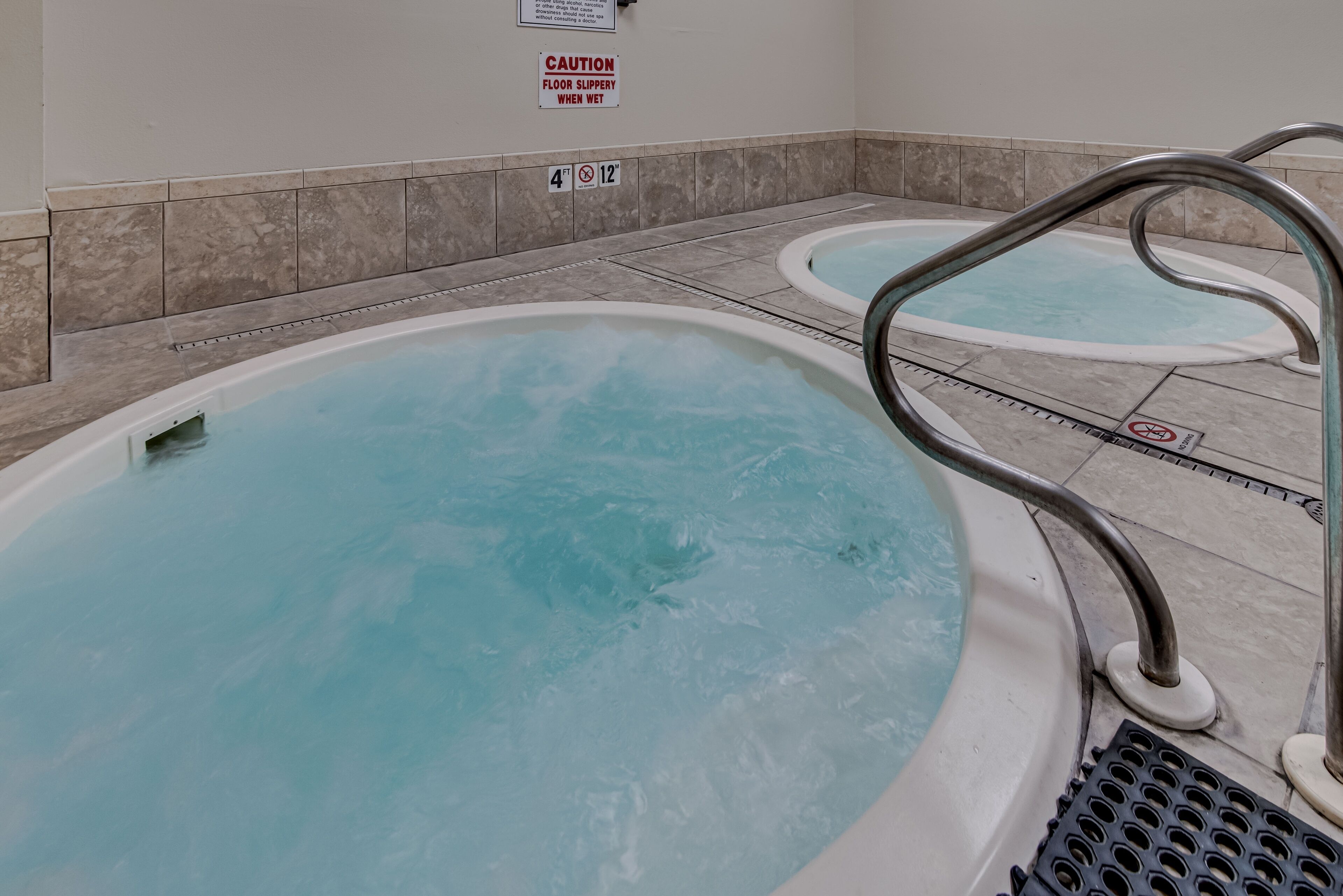 A spa area with two hot tubs and a caution sign about slippery floors.