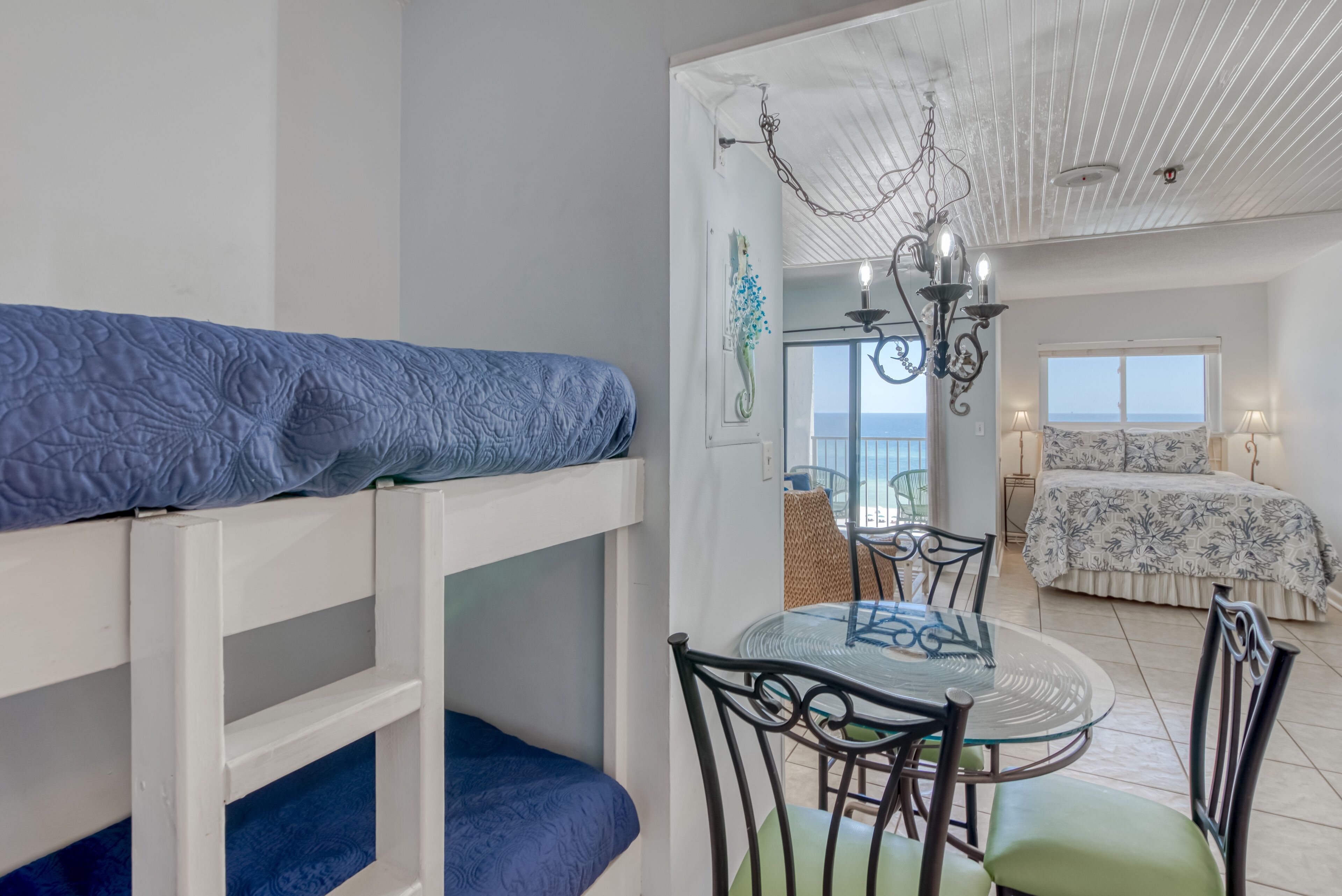 A room with bunk beds, a dining table with chairs, a chandelier, and a bed with a patterned bedspread.