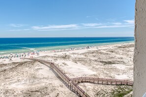 A beach with a wooden boardwalk leading to the shore, sandy dunes, and clear blue water.