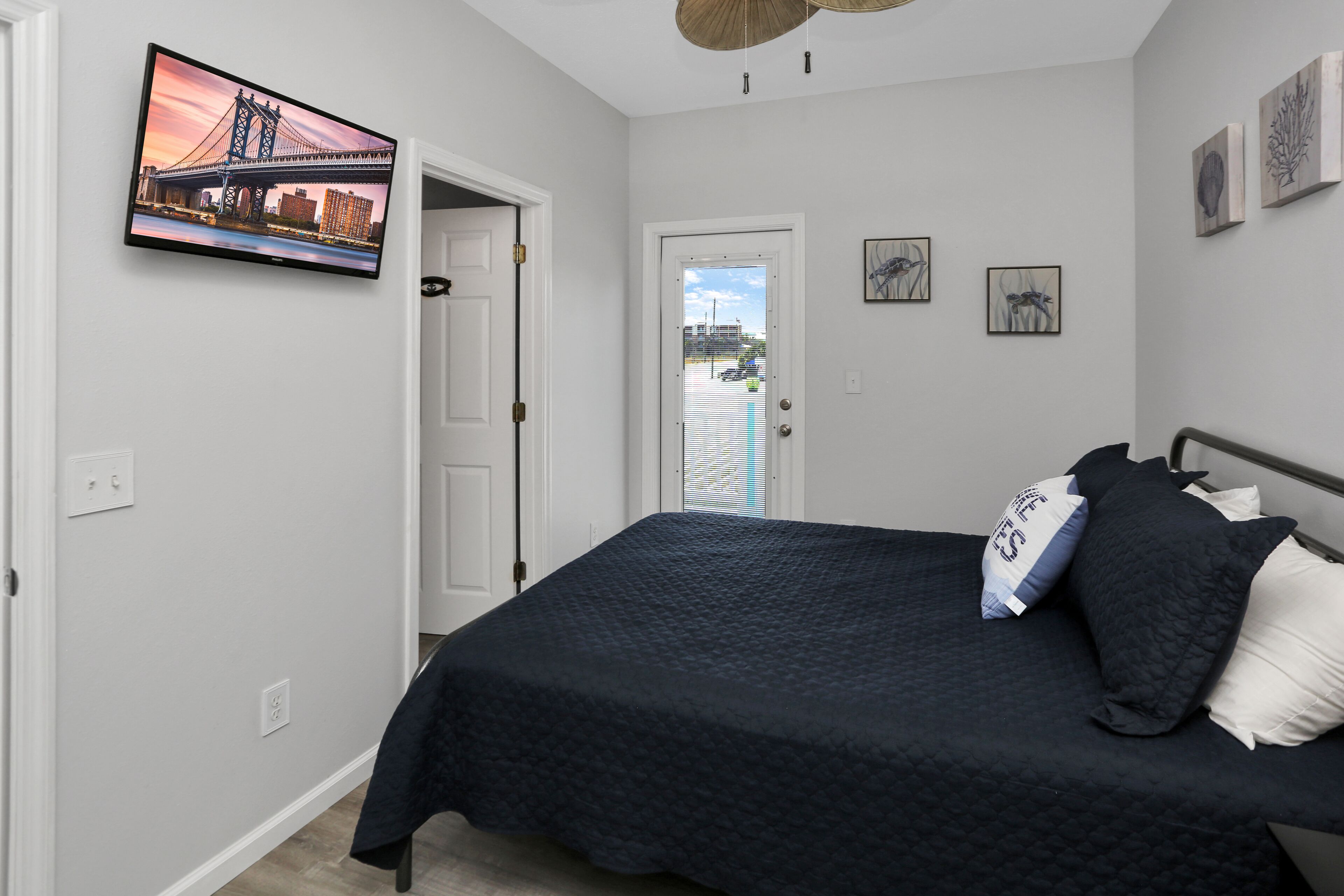 A bedroom with a bed, a TV mounted on the wall, and a door leading to a balcony.