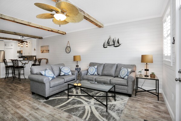Un salon spacieux avec un ensemble de canapés gris, une table basse et un ventilateur de plafond.