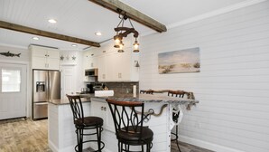A kitchen with white cabinetry, a stainless steel refrigerator, a marble island with bar stools, and a hanging light fixture. - Gulf View, Ground Floor TH on West End of Mexico Beach ~ Set Sail at 5 (Mexico Beach)