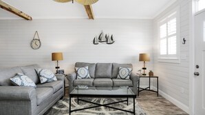 A living room with a gray sofa, two side tables with lamps, a coffee table, a clock, and a wall-mounted sailboat decoration. - Gulf View, Ground Floor TH on West End of Mexico Beach ~ Set Sail at 5 (Mexico Beach)