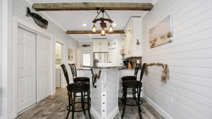 A kitchen with white cabinetry, a central island with bar stools, and a rustic ceiling beam. - Gulf View, Ground Floor TH on West End of Mexico Beach ~ Set Sail at 5 (Mexico Beach)
